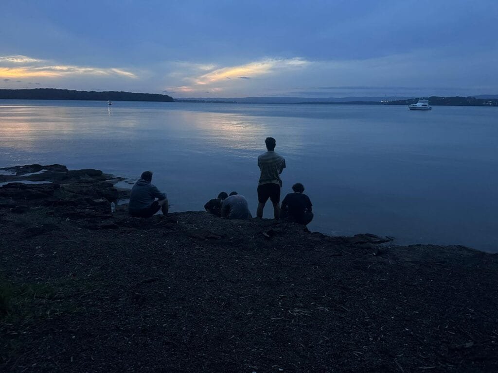 group of 5 friends watches the sun set over lake macquarie